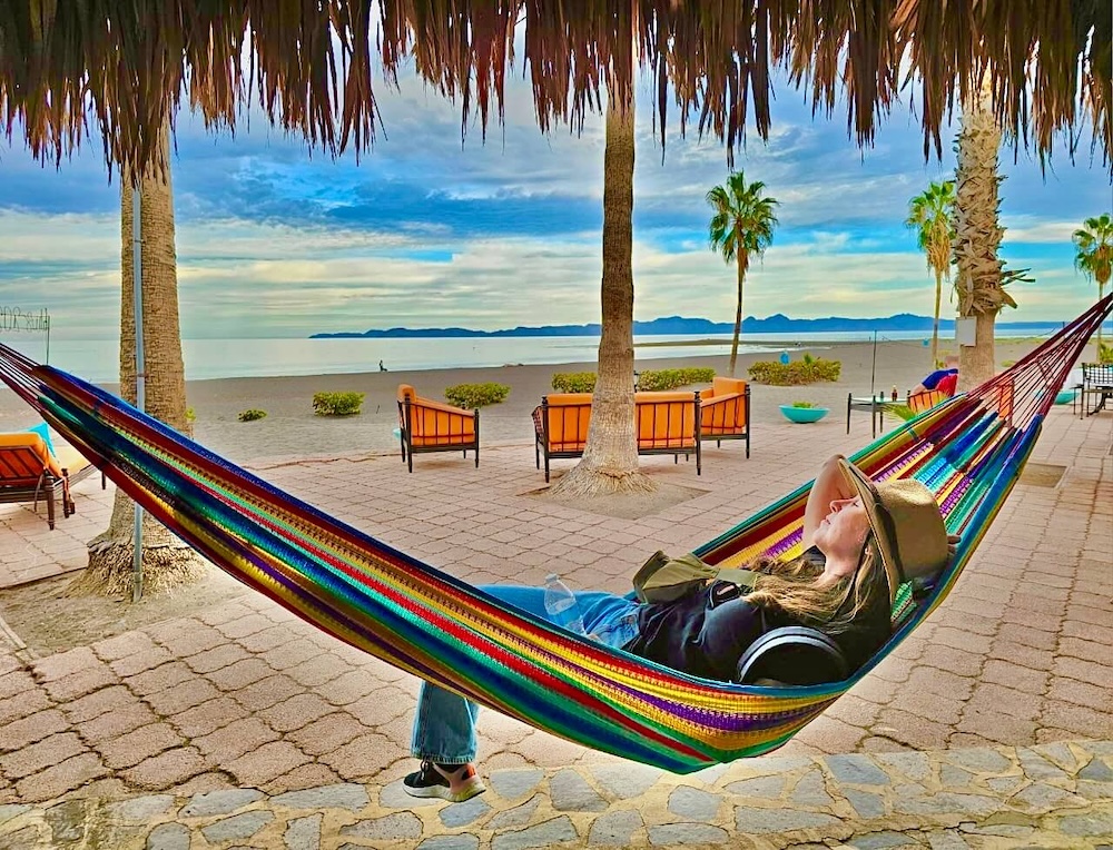 A woman relaxes on a rainbow-colored hammock on the beach in loreto.