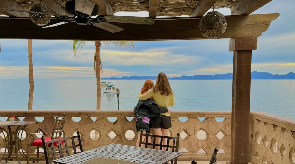 a mom and daughter look out onto the gulf of mexico from the patio of the hotel la mision in loreto