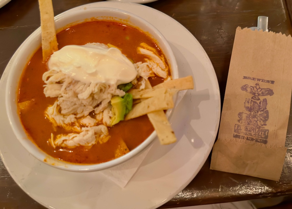 a bowl of tortilla soup at el zopilote in loreto, with chicken, avocado, creme and tortilla strips in a red broth.