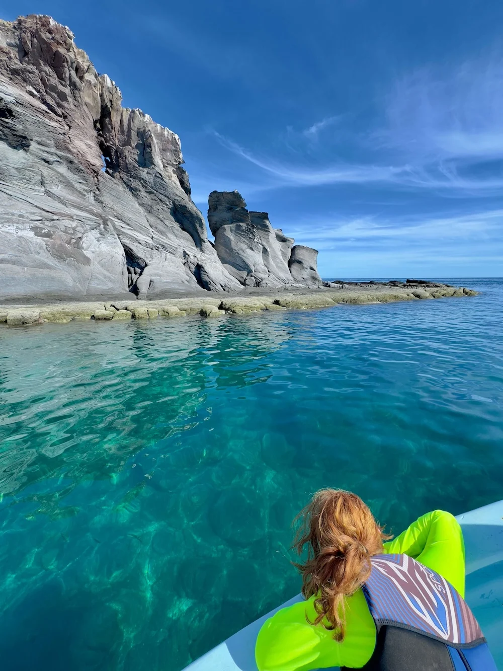 a girl looks over the side of a boat to look for fish in the clear water of the sea of cortez off or loreto
