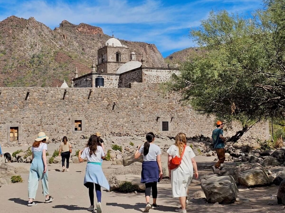 A group of tens walk past rocks and cypress trees toward mission javier in the foothills above loreto.