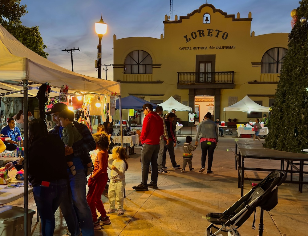people shop for souvenirs at dusk at stalls set up on loreto's main plaza.