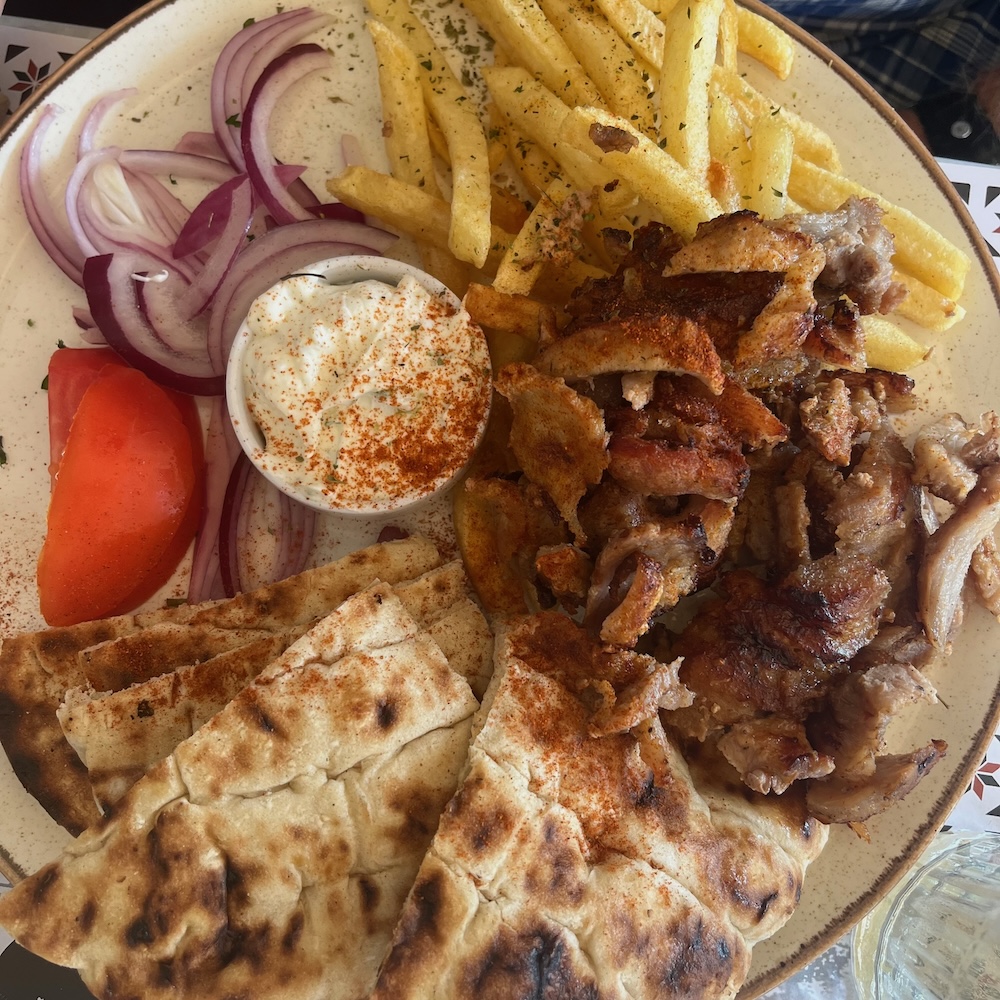 a typical gyro platter in athens, covered in meat, tomato, onions, pita bread, tzatziki and french fries.
