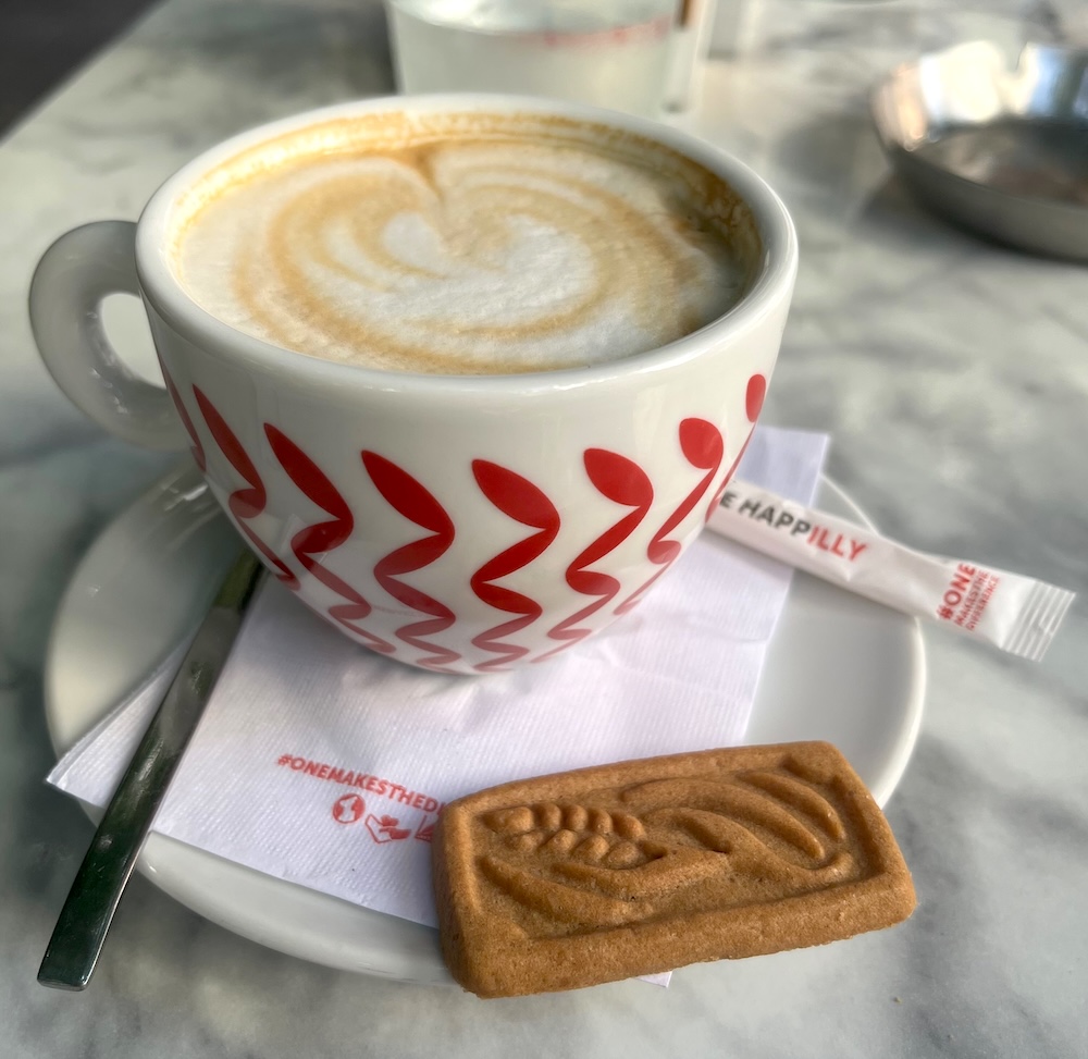 A latter at diplo cafe in exarchia is serve in a red and white mug with a straw of sugar and a cookie.