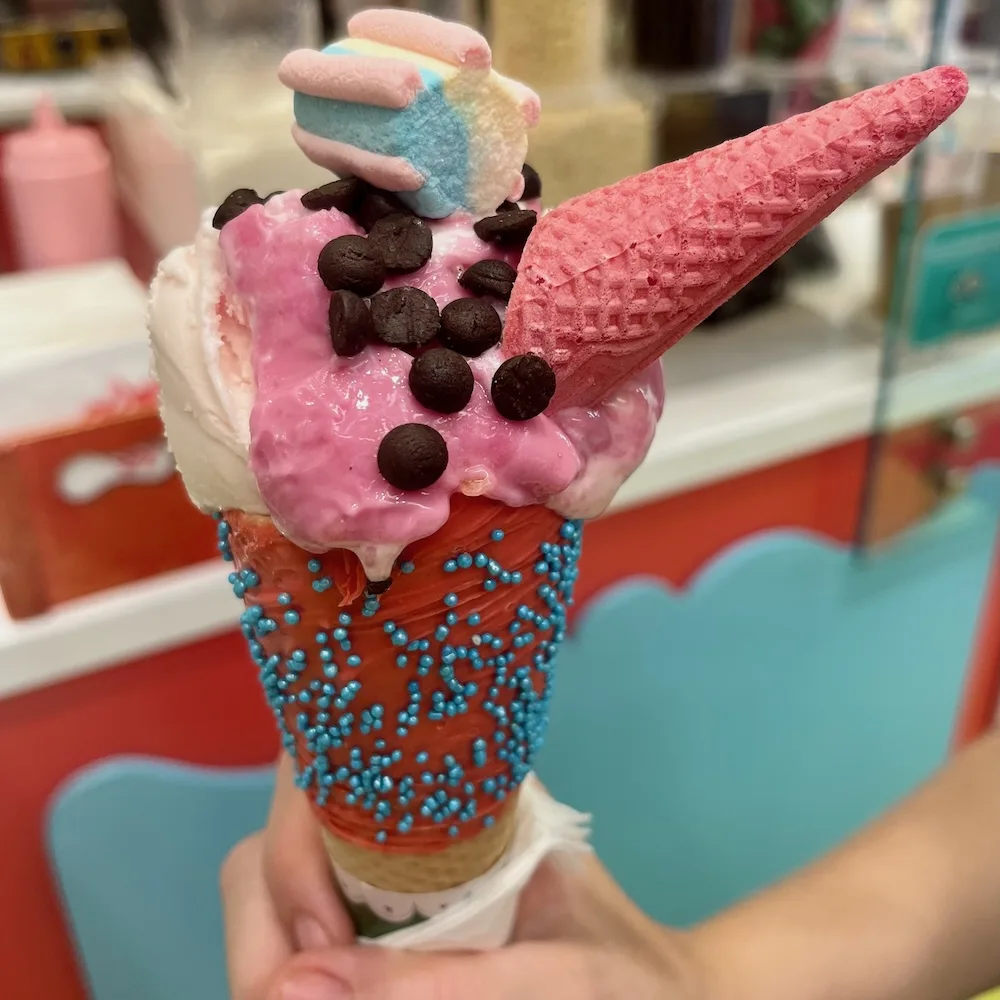 a colorful and elaborate ice cream cone from hans & gretel in monastiraki has pink ice cream, cookie bits, a pastel marshmello and a tiny pink cone hat.