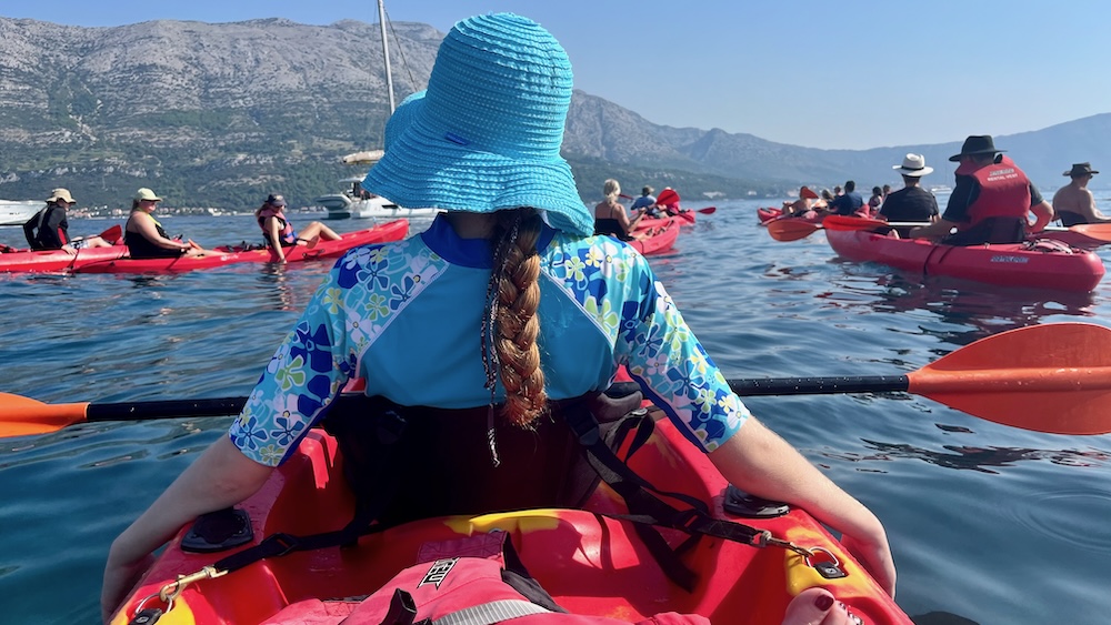 a fleet of kayaks ready to head away from korcula, with mountains in the view across the bay.