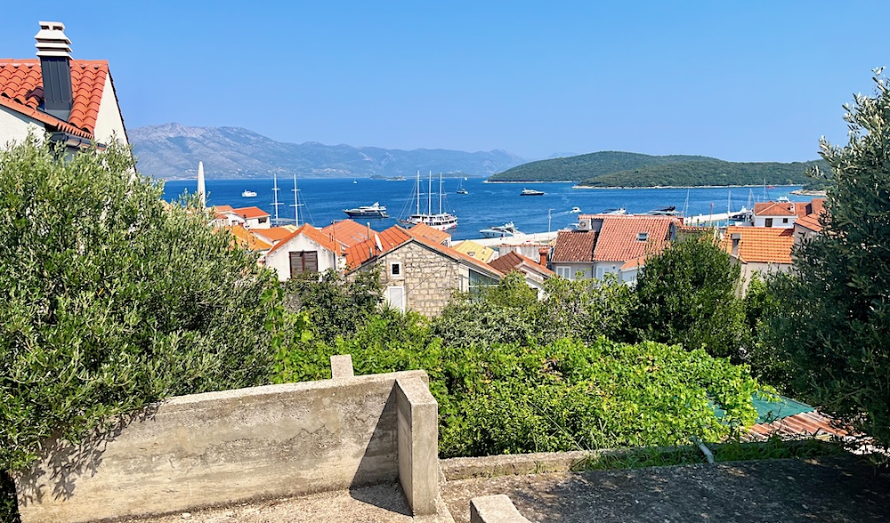 a view of korcula's stone house, red roofs, blue sea and gray mountains from atop a hill.  the island is a fun mediterannean cruise stop with teens.