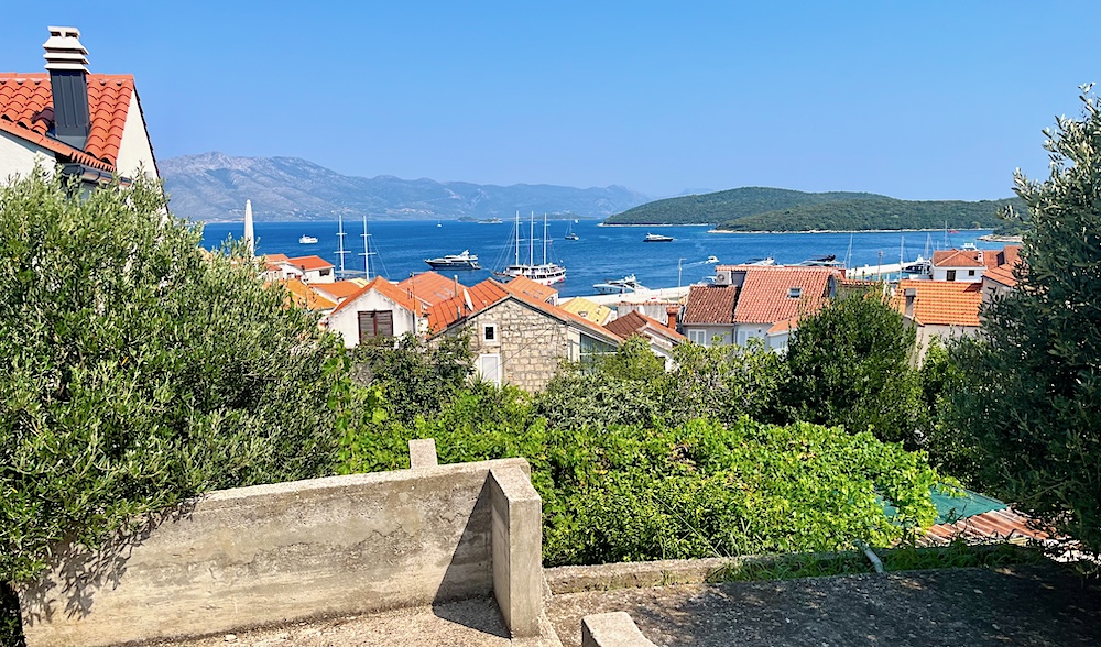 A view of korcula's stone house, red roofs, blue sea and gray mountains from atop a hill. The island is a fun mediterannean cruise stop with teens.