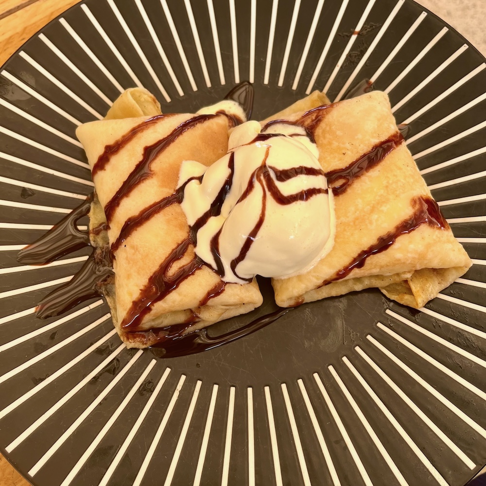 Palacinke, croatian crepes on an art-deco black-and-white plate with vanilla ice cream and chocolate sauce.