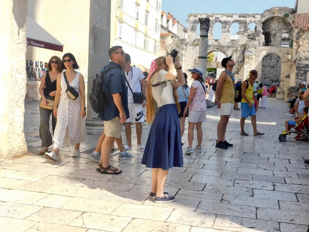 a girl photographs split's old town with marble floors below, roman arches behind and 18th century apartments next door. 