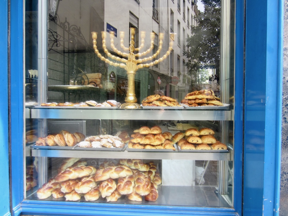 A bakery in paris' jewish quarter has a menorah and several kinds of bread in its window. The neighborhood is a cheap and fun place to eat with kids.